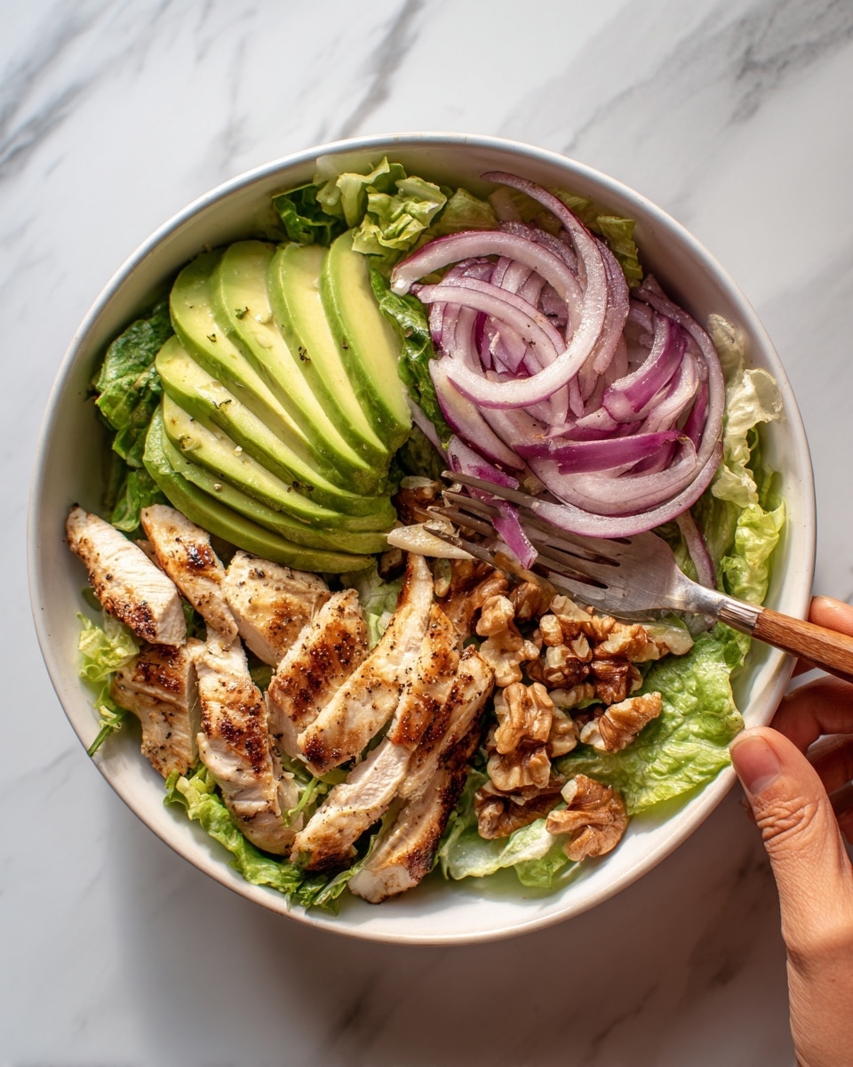 A white bowl filled with a fresh salad sits on a white marbled surface. The salad has four layers visible from the top: the bottom layer is a bed of light green lettuce leaves with a leafy, slightly rough texture covering the whole bowl. On top of this are thin slices of pale green avocado arranged in a fan shape on one side. Next, there are light red, thinly sliced onions scattered evenly with a slightly translucent texture. Throughout the salad, grilled chicken strips with a light golden brown color and faint grill marks are spread, some pieces whole and some slightly angled. A few shelled walnuts with a textured, uneven brown surface are sprinkled here and there for crunch. A woman’s hand is holding a fork with a wooden handle near the corner of the bowl. Photo taken with an iphone --ar 4:5 --v 7