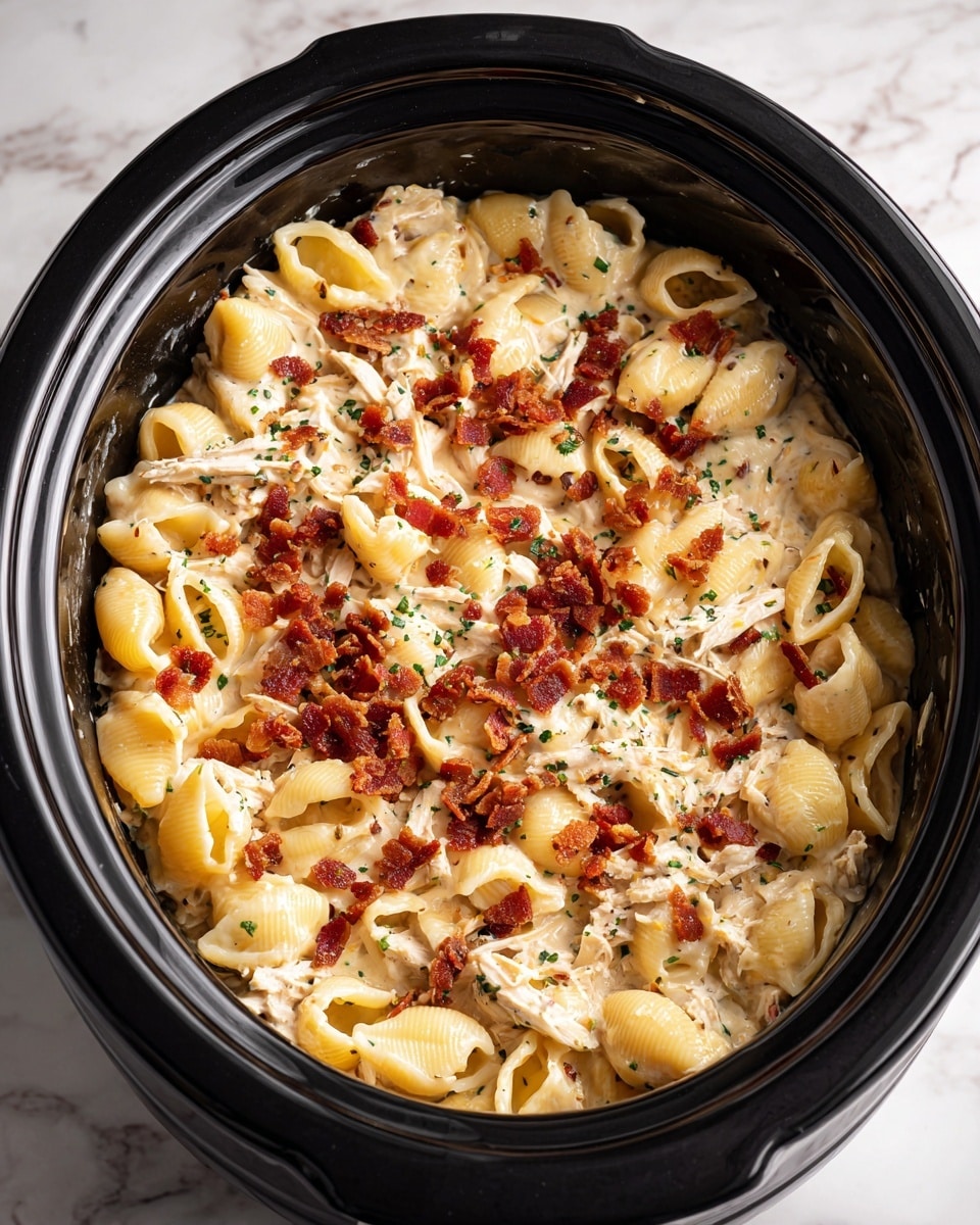A large black slow cooker is filled with creamy yellow pasta shells mixed with shredded light-colored chicken, all coated in a thick white sauce mixed with herbs. On top, there are small crispy reddish-brown bacon pieces scattered across the surface, adding a crunchy texture and rich color contrast to the soft pasta and sauce. The pasta and chicken blend smoothly, while the bacon adds a rough, uneven texture on top. The cooker sits on a white marbled surface. photo taken with an iphone --ar 4:5 --v 7