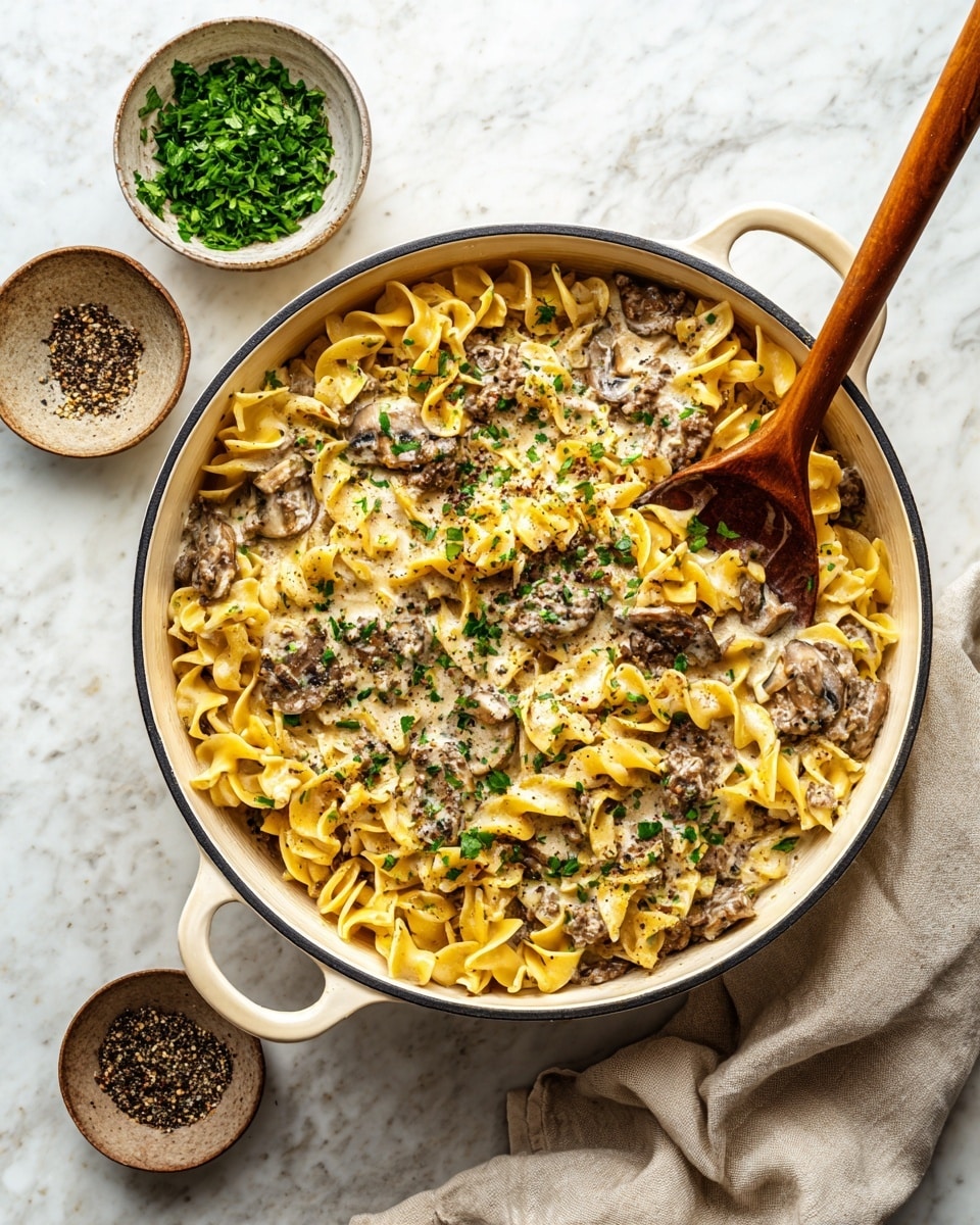 A white pot filled with creamy beef stroganoff layered with twisted yellow egg noodles and tender slices of brown mushrooms, all coated in a light beige sauce with bits of cooked ground beef; the dish is sprinkled with small pieces of fresh green parsley on top. A wooden spoon rests on the right side inside the pot. The pot sits on a white marbled surface, with two small bowls placed nearby – one with chopped green herbs and the other with black and white pepper. A light beige cloth is casually folded beside the pot. Photo taken with an iphone --ar 4:5 --v 7