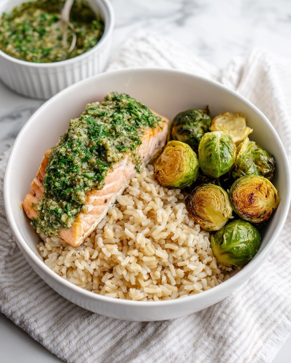 A white bowl contains three main layers of food placed separately. On the bottom left, there is a fluffy layer of cooked brown rice with a light tan color and soft texture. On the bottom right, a group of roasted Brussels sprouts with bright green outer leaves and some browned, crispy spots. On the top left, a piece of light pink salmon topped with a chunky, green herb sauce that looks fresh and vibrant. The bowl sits on a white marbled surface, with a light striped cloth partially visible below it. In the background, there is a white bowl with more green herb sauce. Photo taken with an iphone --ar 4:5 --v 7