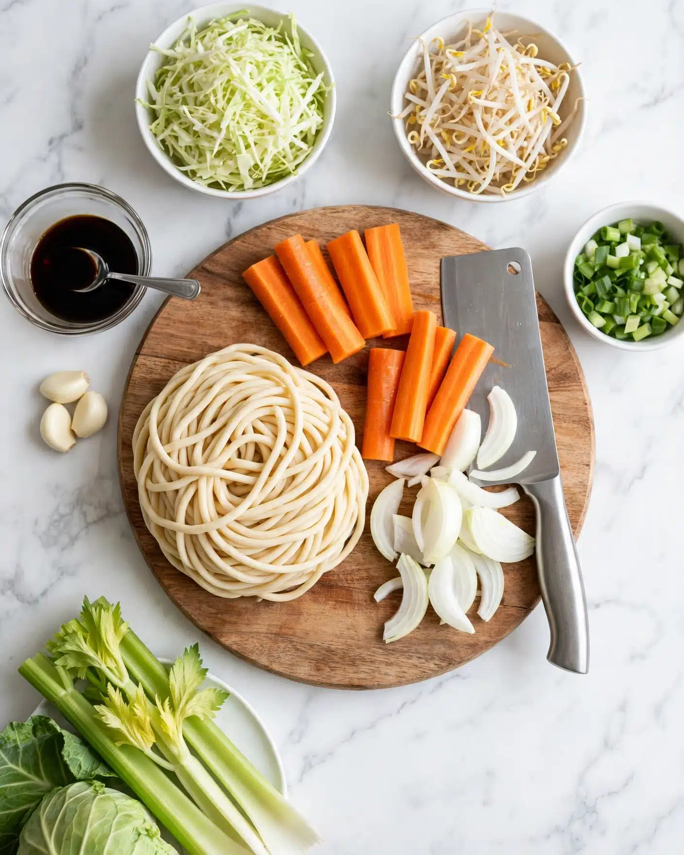 Summer Veggie Stir-Fry with Noodles Recipe 4 The image shows a round wooden board on a white marbled surface with fresh ingredients arranged neatly. On the left side, there is a large round portion of thick uncooked noodles that are creamy in color and have a soft texture. Next to it, there are three peeled garlic cloves, and a small clear glass bowl with dark soy sauce and a spoon inside. On the board, large bright orange carrot sticks are arranged in small piles, while white onion slices are placed beside the carrots on the right. A large silver cleaver knife rests near the vegetables. Surrounding the board, there are small white bowls filled with shredded light green cabbage, cream-colored bean sprouts, and green onions. In the bottom left corner, there is a white plate holding whole green celery stalks and cabbage leaves. The setting is clean and bright, with fresh, crisp ingredients ready to be cooked. Photo taken with an iphone --ar 4:5 --v 7