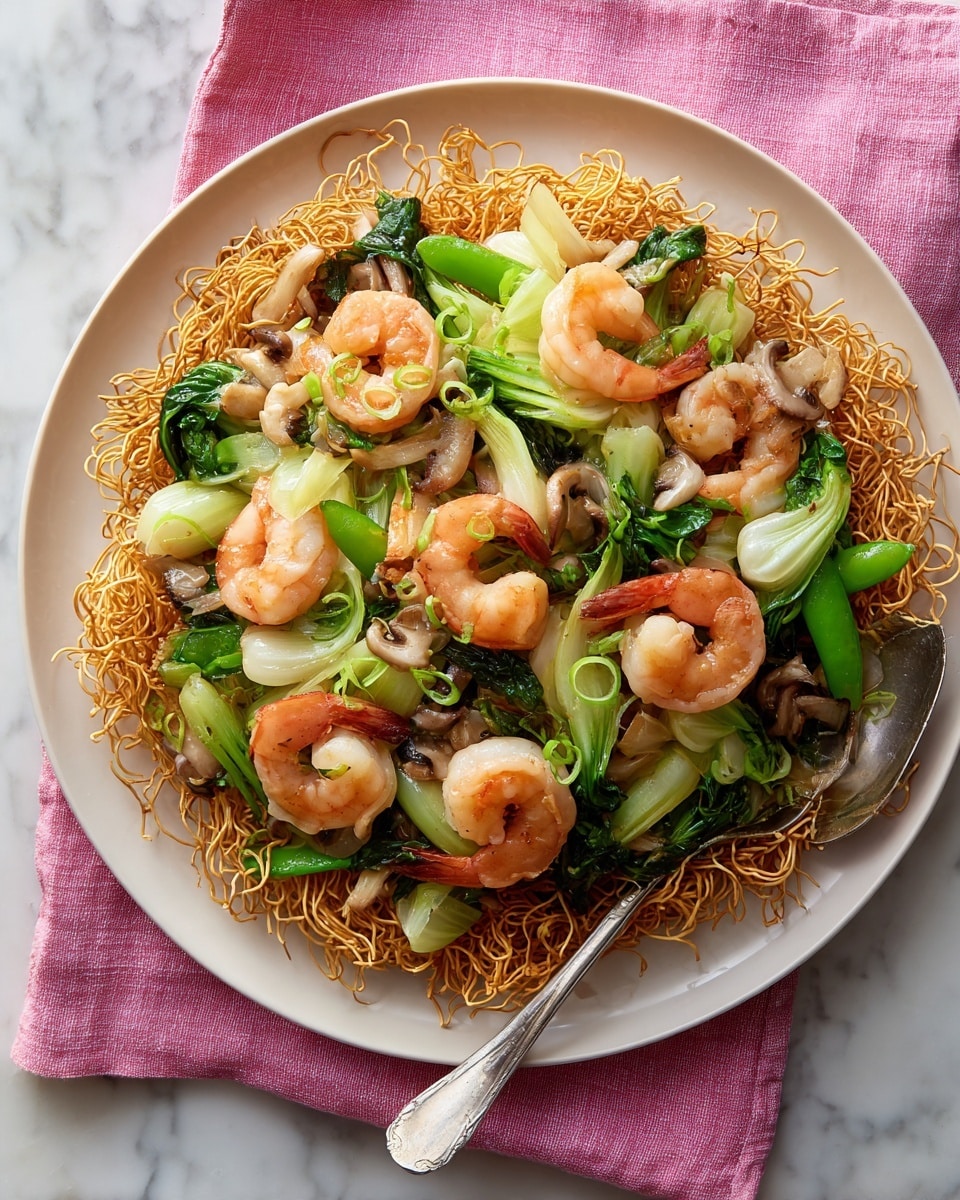 This dish shows a white plate filled with a single crispy golden-brown noodle nest layer that forms the base. On top of the noodles is a colorful mix of vegetables like green snap peas, light green bok choy, and white long mushrooms with small brown tops. Bright pink shrimp with curled tails are scattered evenly across the vegetable layer. The textures vary from crispy noodles, tender shrimp, and fresh, glossy vegetables. A silver fork and spoon rest on the right side of the plate. The plate is placed on a pink cloth over a white marbled surface. photo taken with an iphone --ar 4:5 --v 7