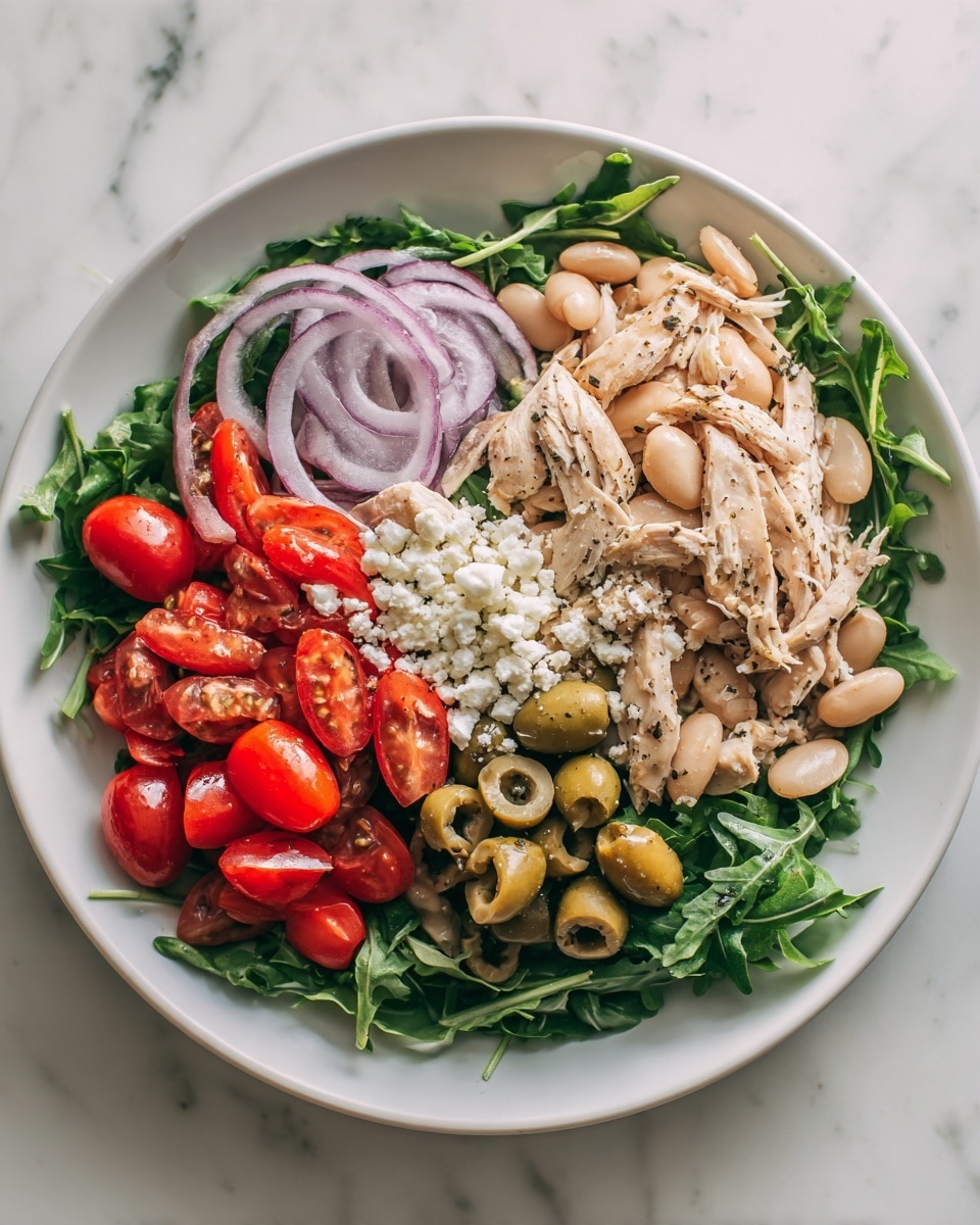 A white round plate filled with a fresh salad layered with green arugula leaves forming the base. On top, there are light beige white beans spread evenly, halved bright red cherry tomatoes, and slices of green olives arranged around the salad edges. Thin, curved rings of purple-red onion are scattered on top, along with crumbled white cheese pieces throughout. There are chunks of light tan shredded chicken mixed in, all seasoned with a sprinkle of black pepper. The whole plate sits on a white marbled surface. Photo taken with an iphone --ar 4:5 --v 7