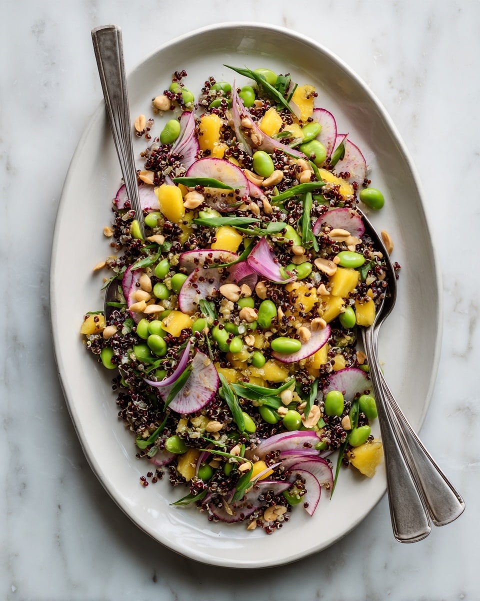 The dish is a vibrant salad served on a white oval plate placed on a white marbled surface. The salad has multiple layers including thinly sliced pale pink radish rounds scattered evenly on top and finely chopped dark red or black quinoa spread throughout. Bright green edamame beans are placed in clusters across the salad, while small diced yellow mango pieces add pops of golden color. Thin slices of red onion with translucent white centers and purple edges are mixed in. Peanuts are sprinkled generously over the top, adding a light tan color and a crunchy texture. Two silver serving spoons rest inside the plate on opposite sides. Photo taken with an iphone --ar 4:5 --v 7