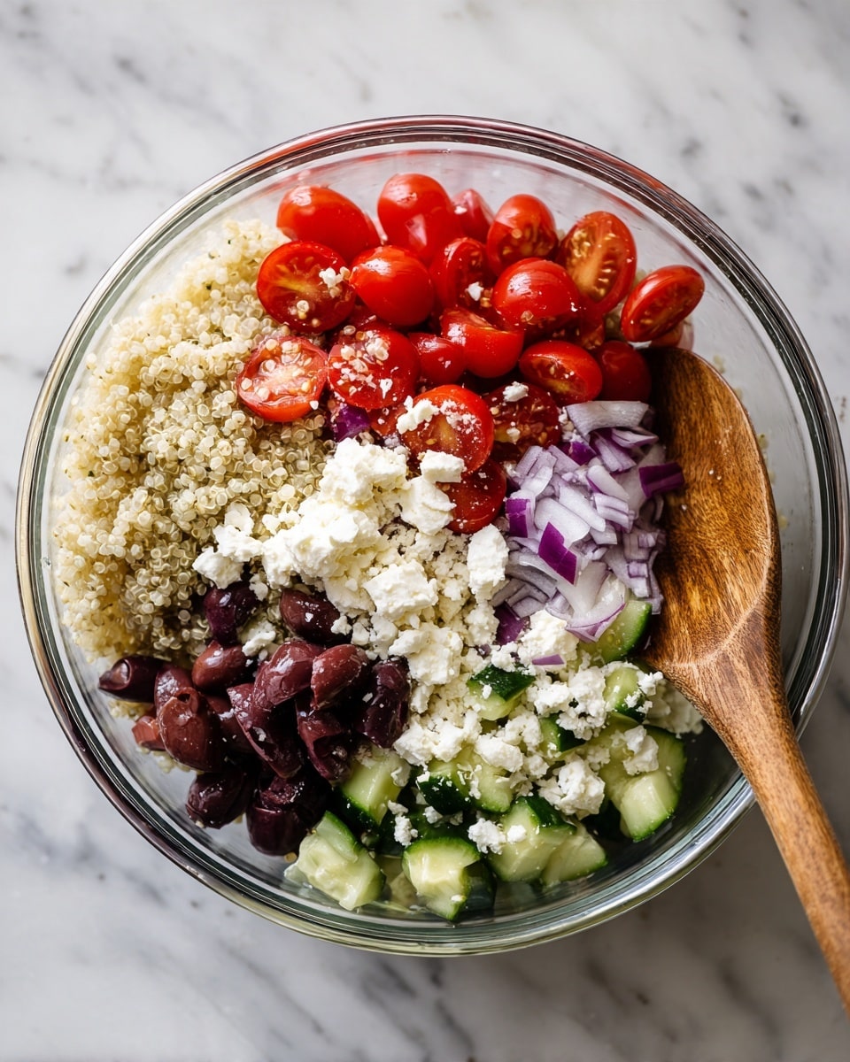 A clear glass bowl filled with a colorful salad made of four main visible layers: small round red cherry tomatoes cut in halves, light beige quinoa grains, dark purple sliced olives, thin strands of pale purple onion, and chunks of white cheese crumbled on top. There are also uneven green cucumber pieces mixed throughout. A wooden spoon is partially submerged on the right side, stirring the salad. The bowl sits on a white marbled surface, showing the vibrant freshness of the ingredients. photo taken with an iphone --ar 4:5 --v 7