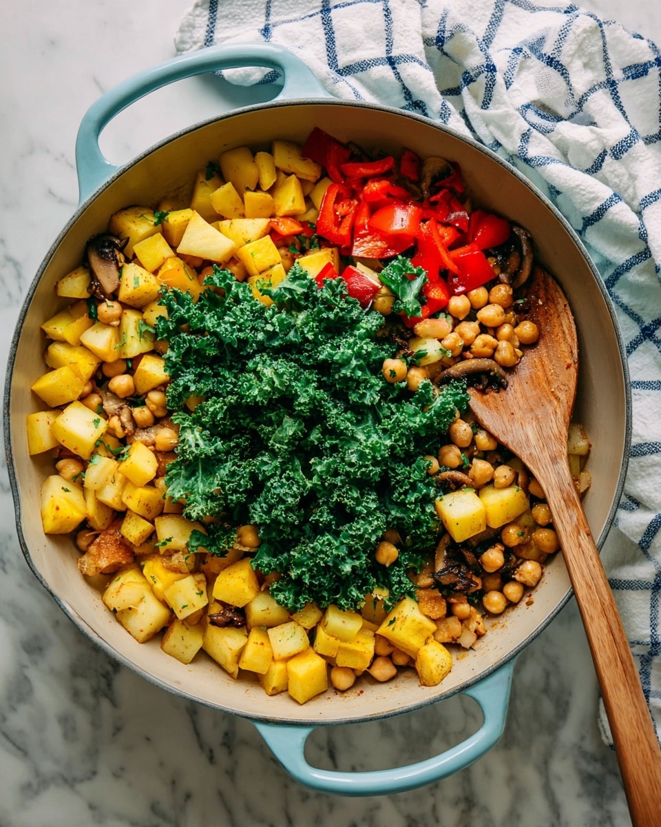 A large light blue pan filled with a mix of cooked vegetables and chickpeas. The dish has four main layers: soft golden-brown cubes of potato and yellow squash evenly spread, bright green curly kale leaves placed on top, small round beige chickpeas scattered around, and slices of dark brown mushrooms mixed throughout. Small pieces of red bell pepper add color across the pan. A wooden spoon rests inside the pan on the right side, and a white cloth with blue checks is in the background on a white marbled surface. photo taken with an iphone --ar 4:5 --v 7