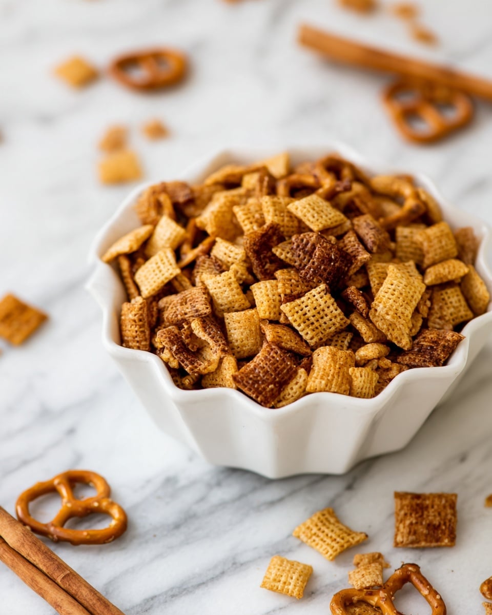 A white scalloped bowl filled with a snack mix that has several layers: the bottom layer consists of golden brown little square cereal pieces with a crunchy texture, scattered throughout are darker brown pretzels in classic twisted shapes, and small bits of cinnamon sticks lay beside the bowl on a white marbled surface. The colors range from light golden to deep brown, and the textures look crunchy and crisp, photo taken with an iphone --ar 4:5 --v 7