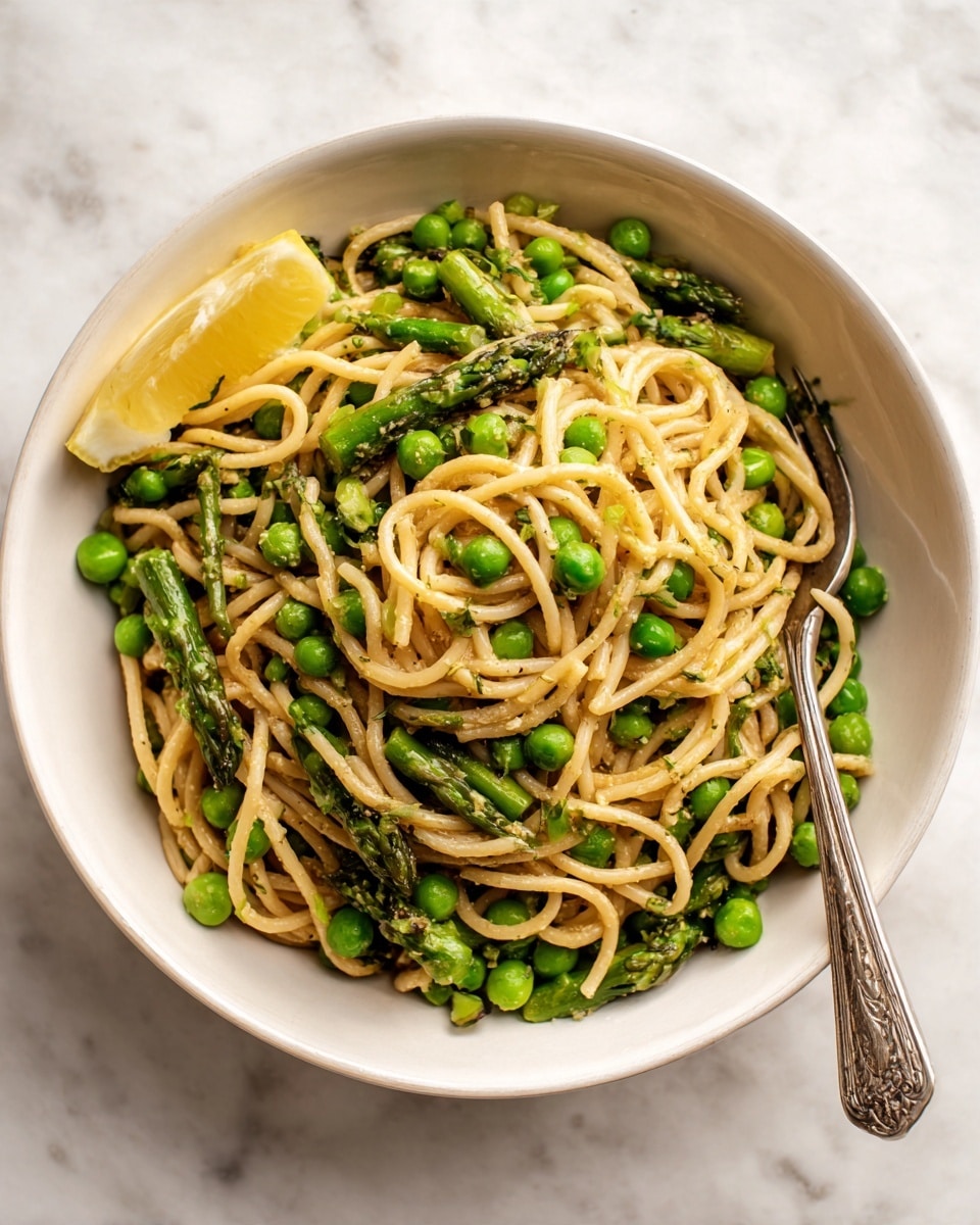 The dish is a white bowl filled with a pasta salad that has long, thin noodles mixed with bright green peas and asparagus pieces. The noodles are light beige and slightly twisted around the vegetables. The peas are round and scattered evenly, while the asparagus is cut into short segments, showing a firm and smooth texture. There is a wedge of lemon on the side of the bowl for garnish. The bowl sits on a white marbled surface with a silver fork placed beside it. Photo taken with an iphone --ar 4:5 --v 7